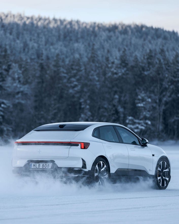 Rear view of Polestar 4 driving on a snowy road with a forest in the background